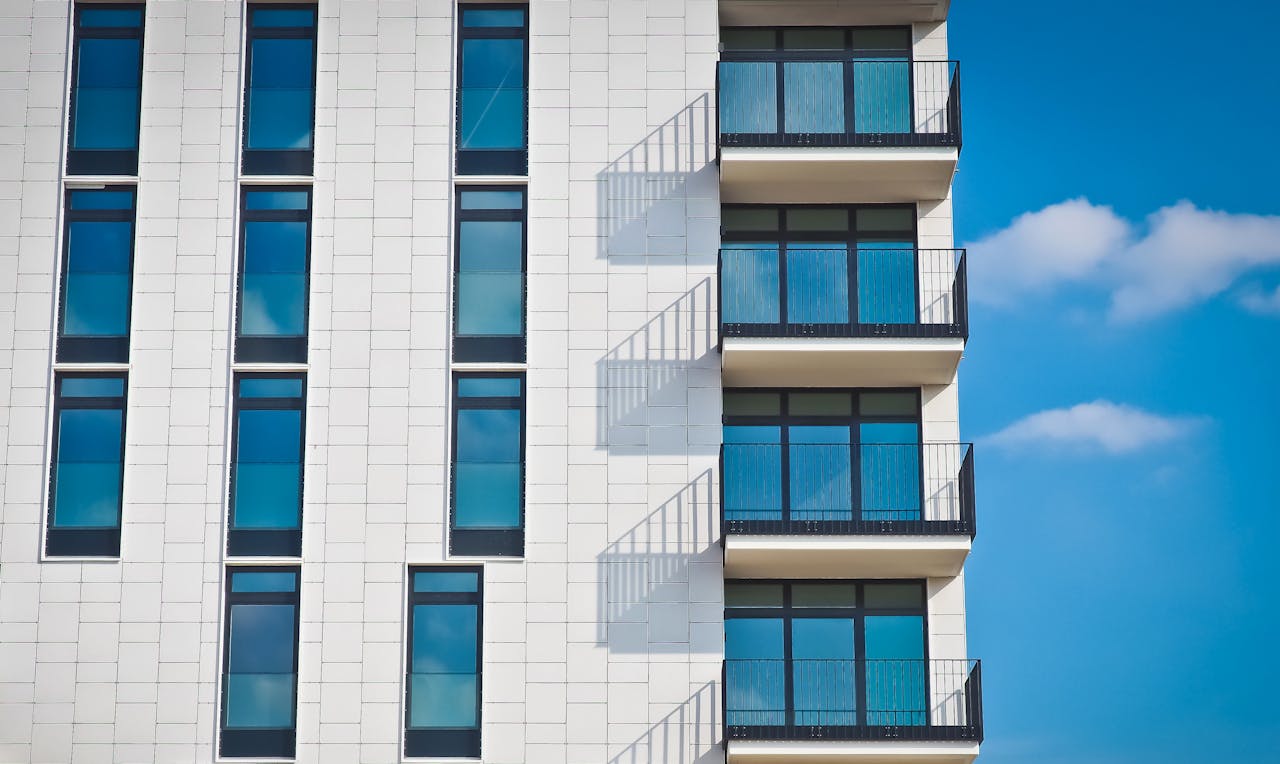 contact-header Contemporary urban apartment building with framed glass windows against clear blue sky.