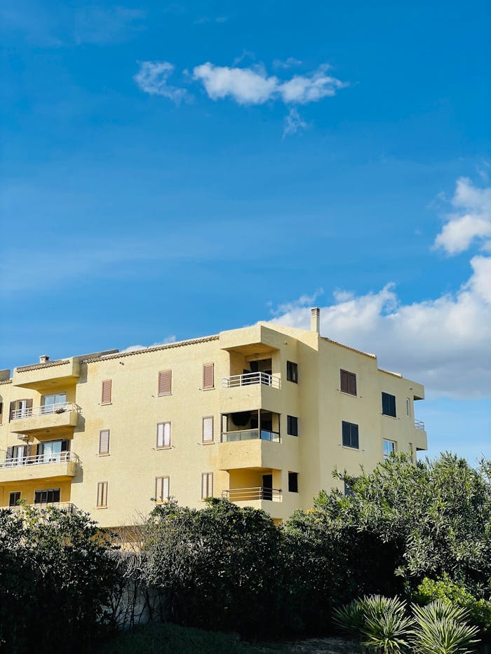 why-choose-us Sunny apartment building with lush greenery against a blue sky.